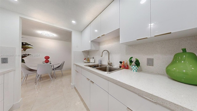 kitchen with tasteful backsplash, white cabinetry, sink, and light tile patterned floors