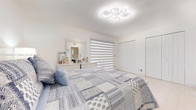 bedroom with a textured ceiling, two closets, and light tile patterned floors