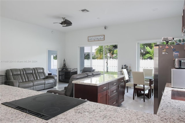 kitchen with light stone countertops, a wealth of natural light, a center island, and black electric stovetop