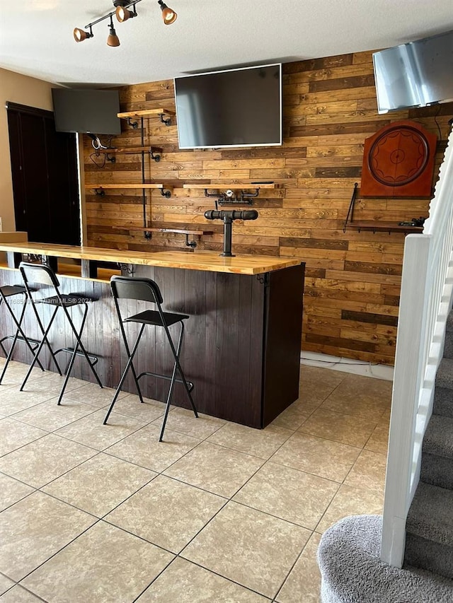 bar featuring light tile patterned flooring, wooden walls, and butcher block countertops