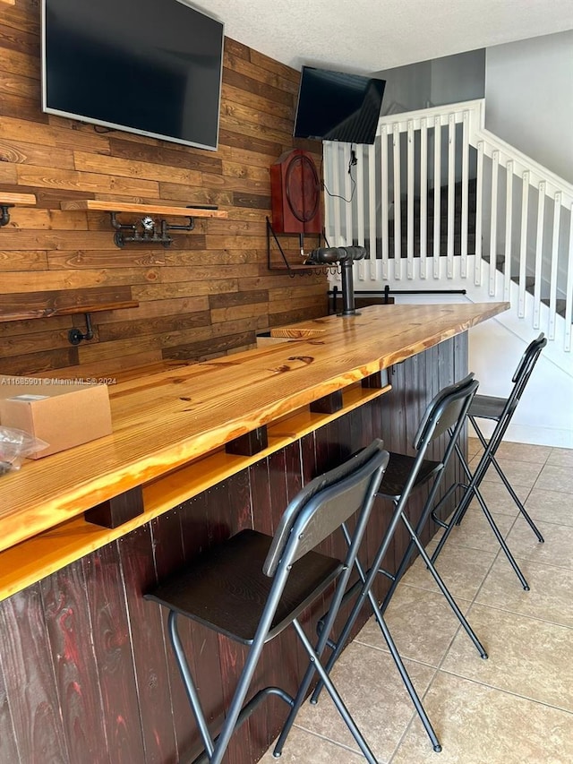 bar with light tile patterned flooring, butcher block counters, and wooden walls