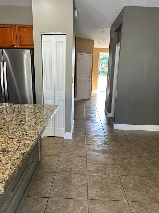 kitchen featuring a textured ceiling, light stone counters, dark tile patterned floors, and stainless steel refrigerator