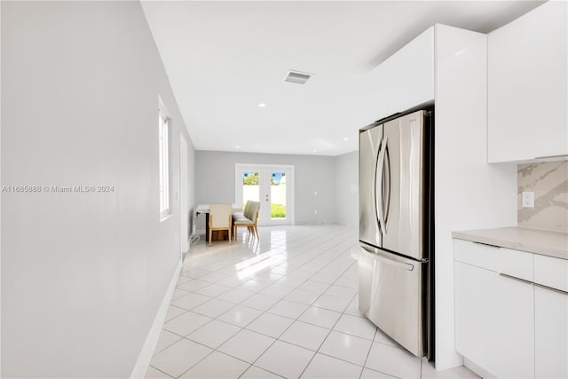 kitchen with decorative backsplash, white cabinetry, light tile patterned floors, and stainless steel refrigerator