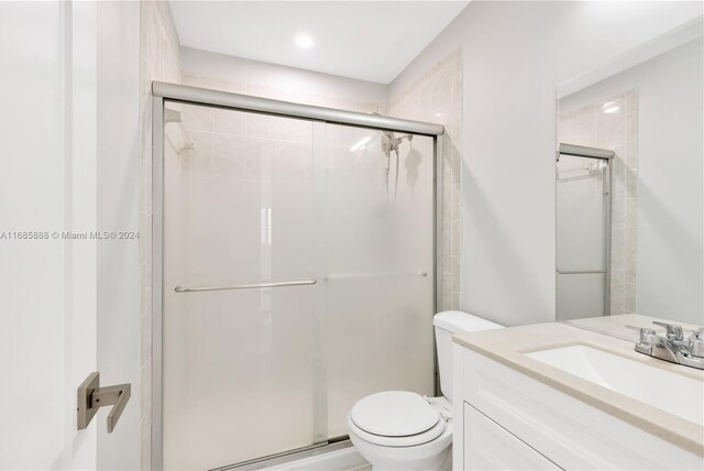 bathroom featuring toilet, vanity, and a shower with door