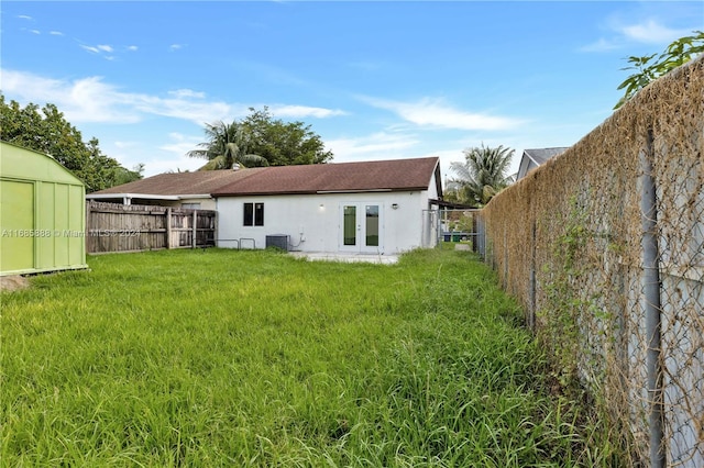 back of property featuring cooling unit, a storage shed, a yard, and french doors