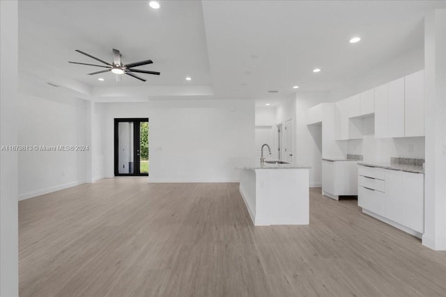 kitchen with sink, white cabinetry, light stone countertops, an island with sink, and light wood-type flooring