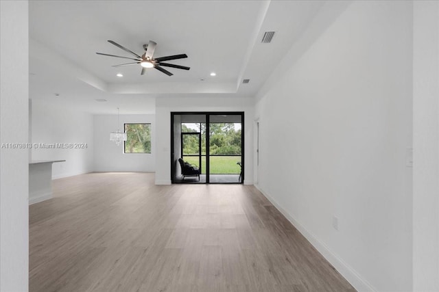 spare room featuring a tray ceiling, ceiling fan with notable chandelier, and light wood-type flooring