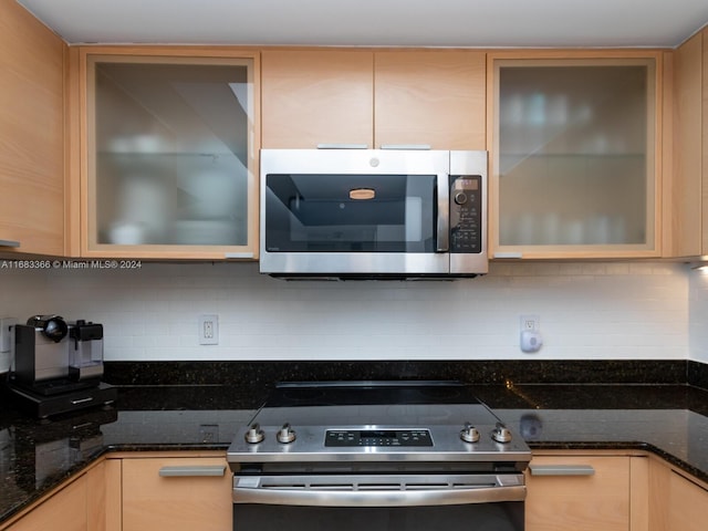 kitchen with light brown cabinetry, stainless steel appliances, and dark stone counters