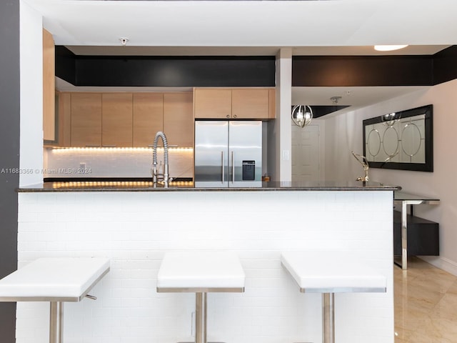 kitchen featuring kitchen peninsula, stainless steel fridge, dark stone counters, a breakfast bar, and sink