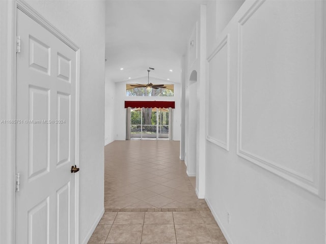 corridor with light tile patterned floors, vaulted ceiling, and baseboards