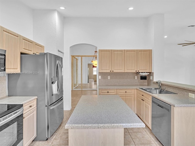 kitchen featuring stainless steel appliances, a sink, light brown cabinets, a towering ceiling, and a kitchen island