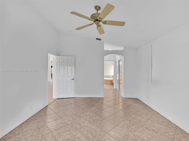 empty room featuring arched walkways, lofted ceiling, ceiling fan, and light tile patterned flooring