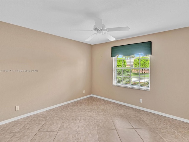 tiled empty room with ceiling fan and baseboards