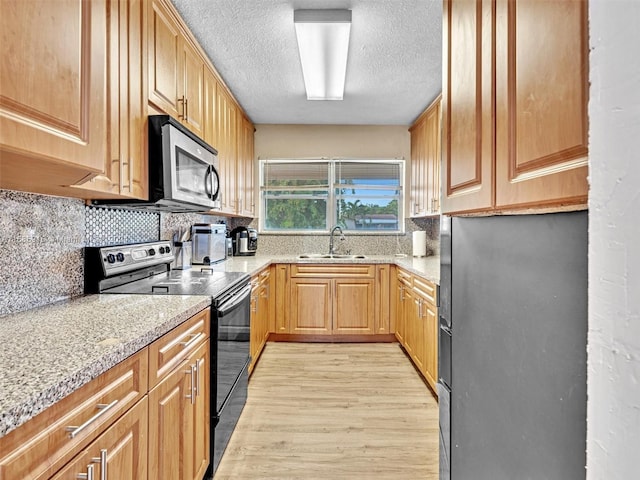 kitchen featuring light stone countertops, sink, electric range, black fridge, and light hardwood / wood-style floors