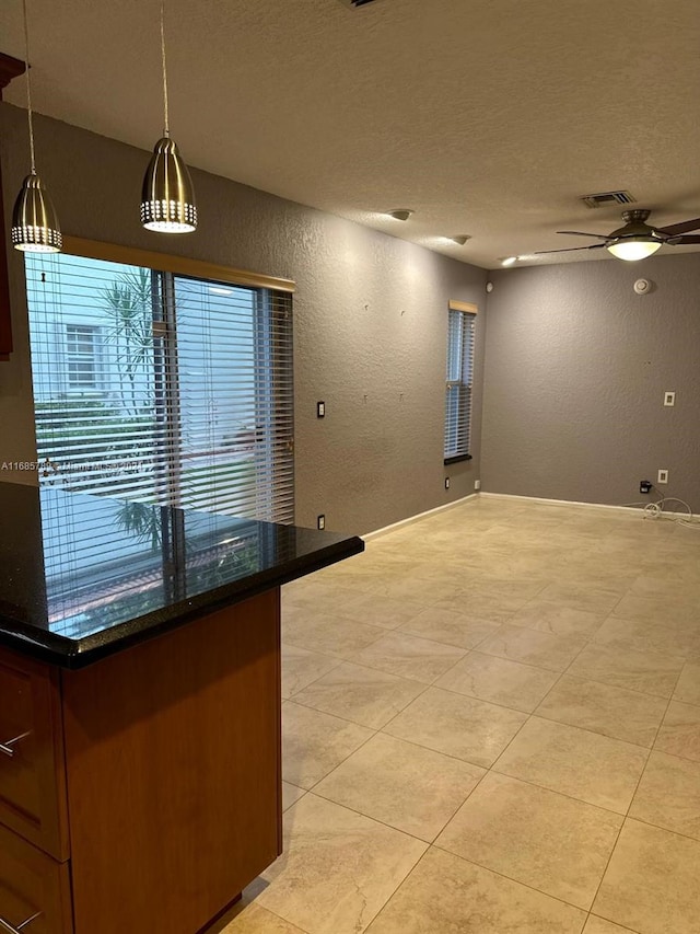 interior space with ceiling fan, light tile patterned floors, a textured ceiling, dark stone countertops, and pendant lighting