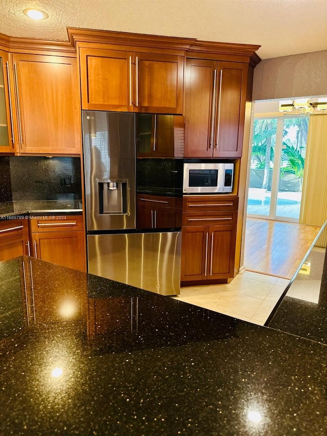 kitchen featuring appliances with stainless steel finishes, light tile patterned flooring, backsplash, a textured ceiling, and dark stone counters