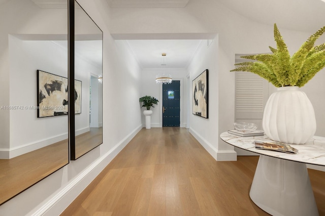 hall featuring a notable chandelier, ornamental molding, and light wood-type flooring