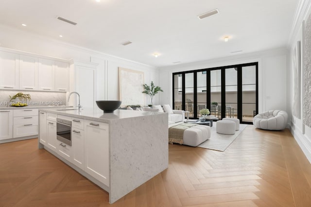 kitchen featuring light parquet flooring, white cabinets, sink, and a center island with sink