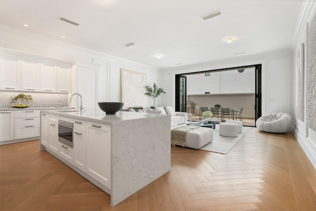 kitchen with light parquet floors, white cabinetry, sink, and an island with sink