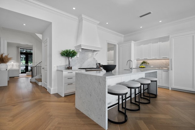 kitchen featuring a kitchen island with sink, white cabinets, light parquet floors, and backsplash