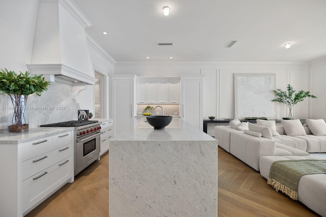 kitchen featuring light parquet flooring, white cabinetry, premium range, and backsplash