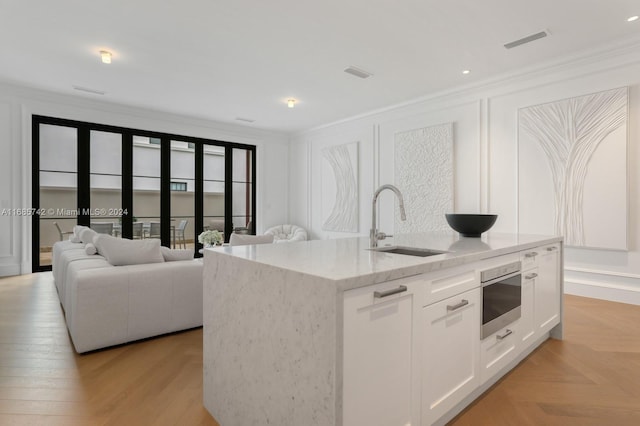 kitchen featuring a center island with sink, light stone counters, white cabinetry, crown molding, and sink