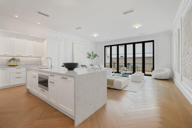 kitchen featuring light parquet flooring, white cabinetry, sink, and an island with sink