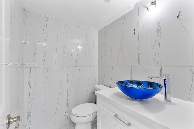 bathroom with tile walls, vanity, a textured ceiling, and toilet