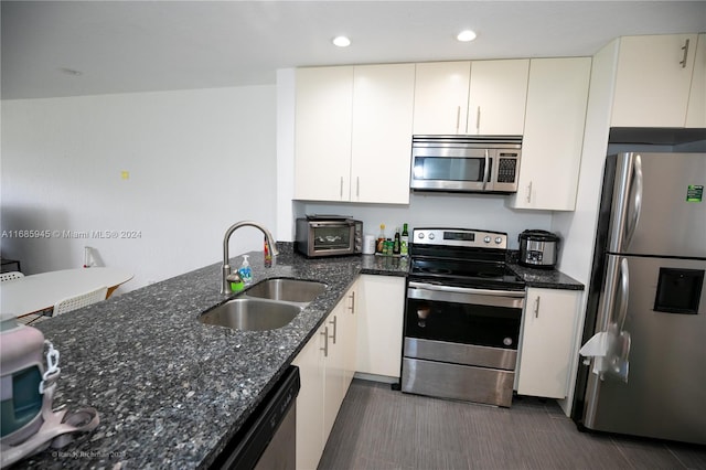 kitchen with sink, kitchen peninsula, stainless steel appliances, dark stone counters, and white cabinets