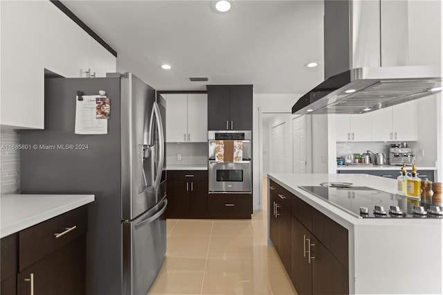 kitchen with wall chimney exhaust hood, light tile patterned floors, backsplash, white cabinetry, and appliances with stainless steel finishes