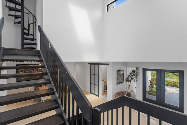 stairway with a barn door, a towering ceiling, and tile patterned floors