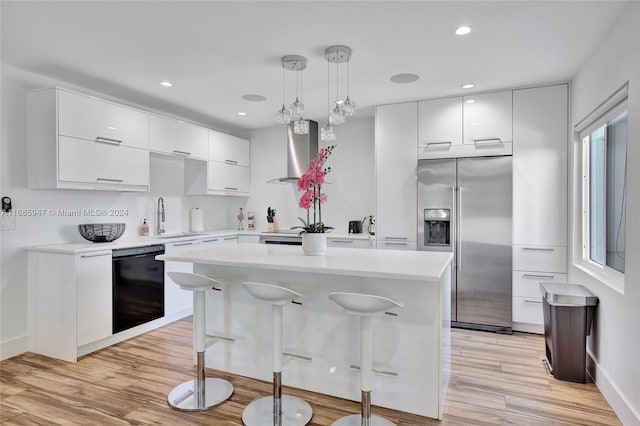 kitchen with wall chimney range hood, light hardwood / wood-style flooring, dishwasher, built in fridge, and decorative light fixtures