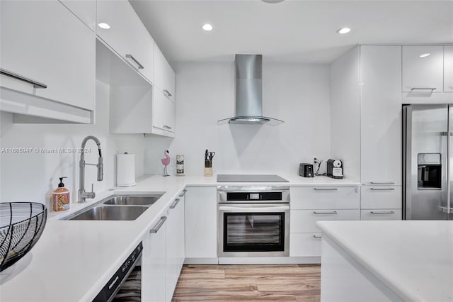 kitchen with white cabinets, black appliances, light hardwood / wood-style floors, wall chimney exhaust hood, and sink