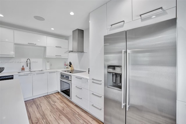 kitchen featuring appliances with stainless steel finishes, sink, light hardwood / wood-style floors, wall chimney exhaust hood, and white cabinets