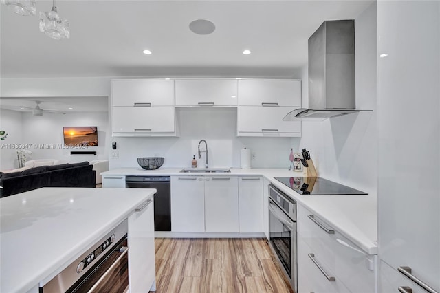 kitchen with wall chimney range hood, white cabinets, black appliances, sink, and decorative light fixtures