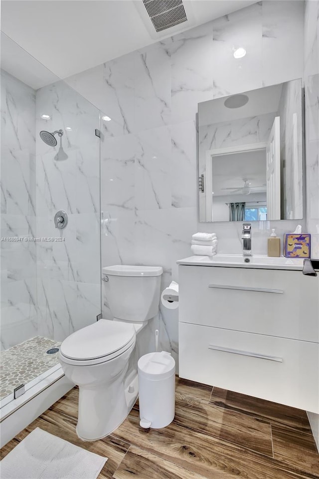 bathroom featuring hardwood / wood-style flooring, tile walls, toilet, tiled shower, and vanity