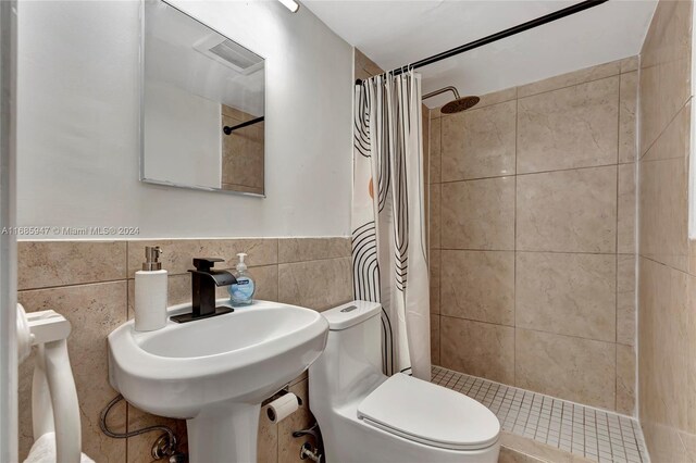 bathroom with a shower with shower curtain, toilet, sink, and tile walls