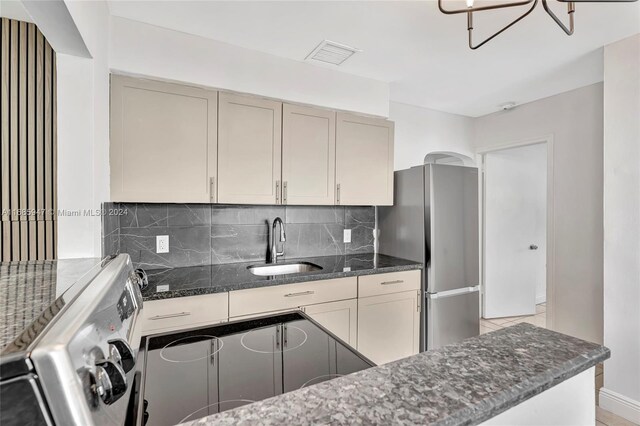 kitchen featuring tasteful backsplash, sink, stainless steel fridge, dark stone counters, and an inviting chandelier