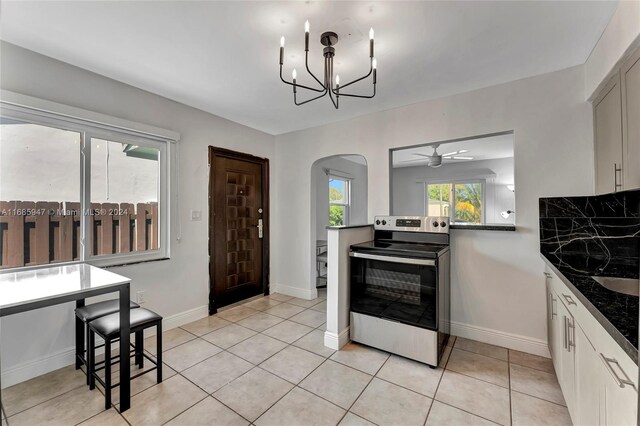 kitchen featuring electric stove, light tile patterned flooring, dark stone counters, and white cabinets