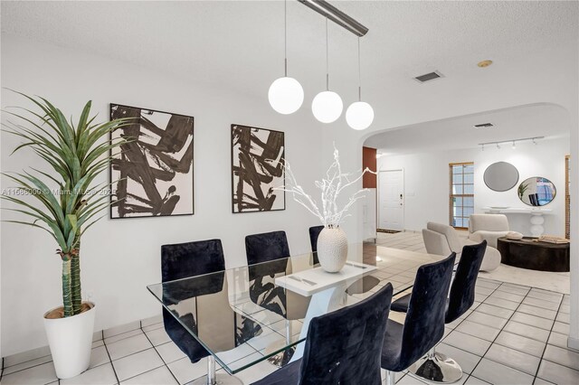 tiled dining room featuring rail lighting and a textured ceiling