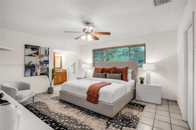 bedroom featuring ceiling fan, ensuite bathroom, a textured ceiling, and light tile patterned floors