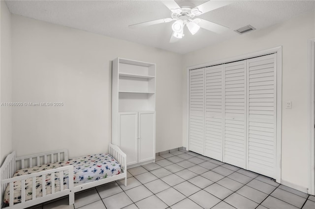 bedroom featuring ceiling fan, light tile patterned floors, a textured ceiling, and a closet