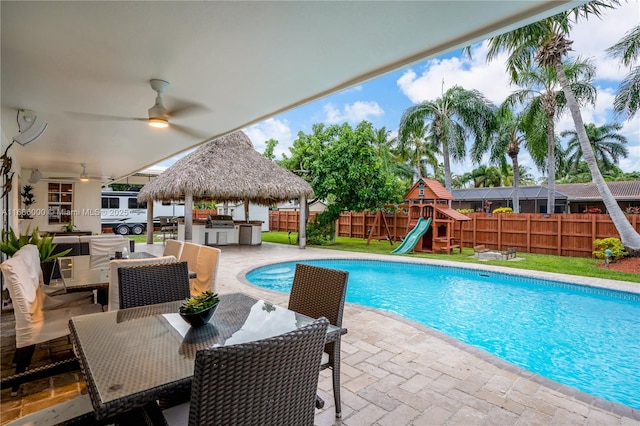 view of pool featuring a playground, an outdoor kitchen, a water slide, ceiling fan, and a patio area