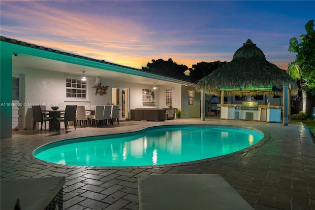 pool at dusk featuring a patio and an outdoor kitchen