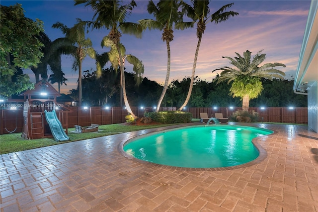 pool at dusk featuring a playground and a patio