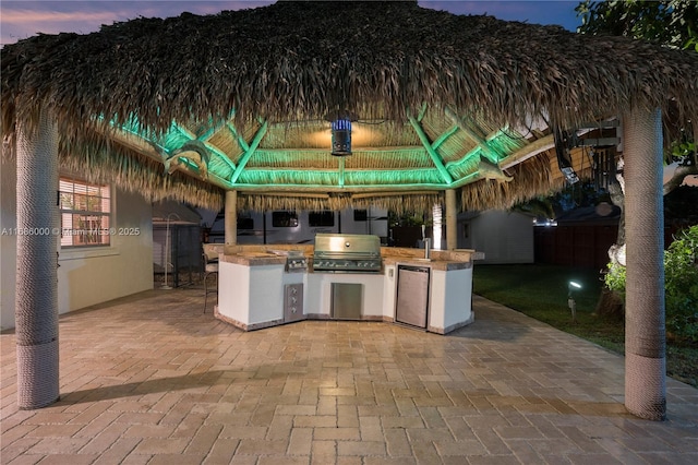 patio terrace at dusk with a gazebo, an outdoor kitchen, and grilling area