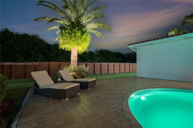 pool at dusk with a patio area and a playground