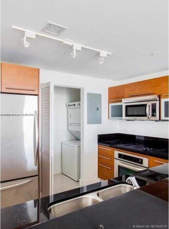 kitchen featuring electric panel, rail lighting, stacked washer and dryer, sink, and stainless steel appliances