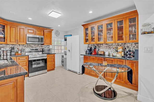 kitchen featuring backsplash, dark stone countertops, sink, light tile patterned floors, and appliances with stainless steel finishes