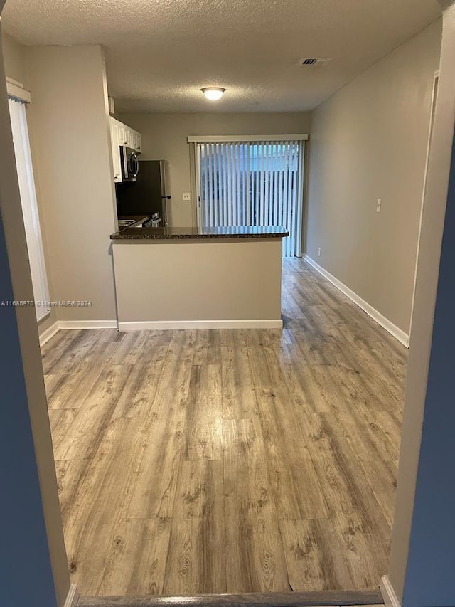 kitchen with appliances with stainless steel finishes, kitchen peninsula, white cabinetry, and light hardwood / wood-style floors